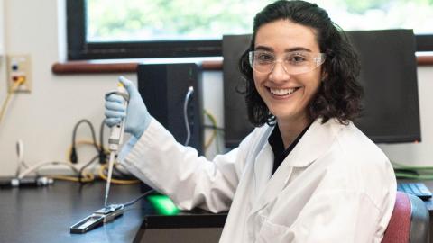 Erica Fuhrmeister smiles holding a micropipet in a lab.