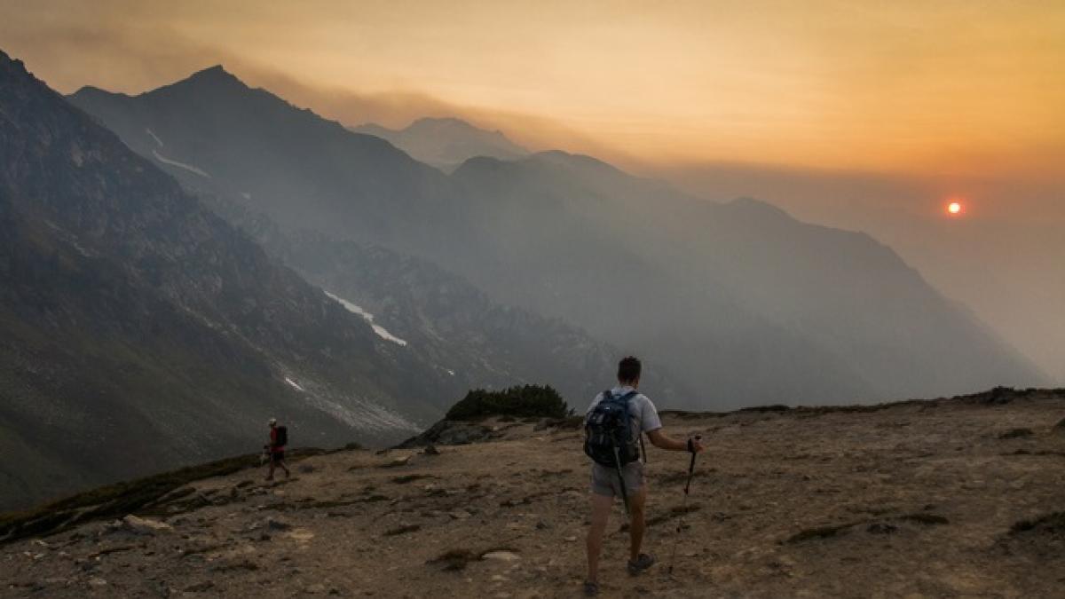 A smoky sunset with mountains and a valley in the background and a hiker facing away in the foreground.