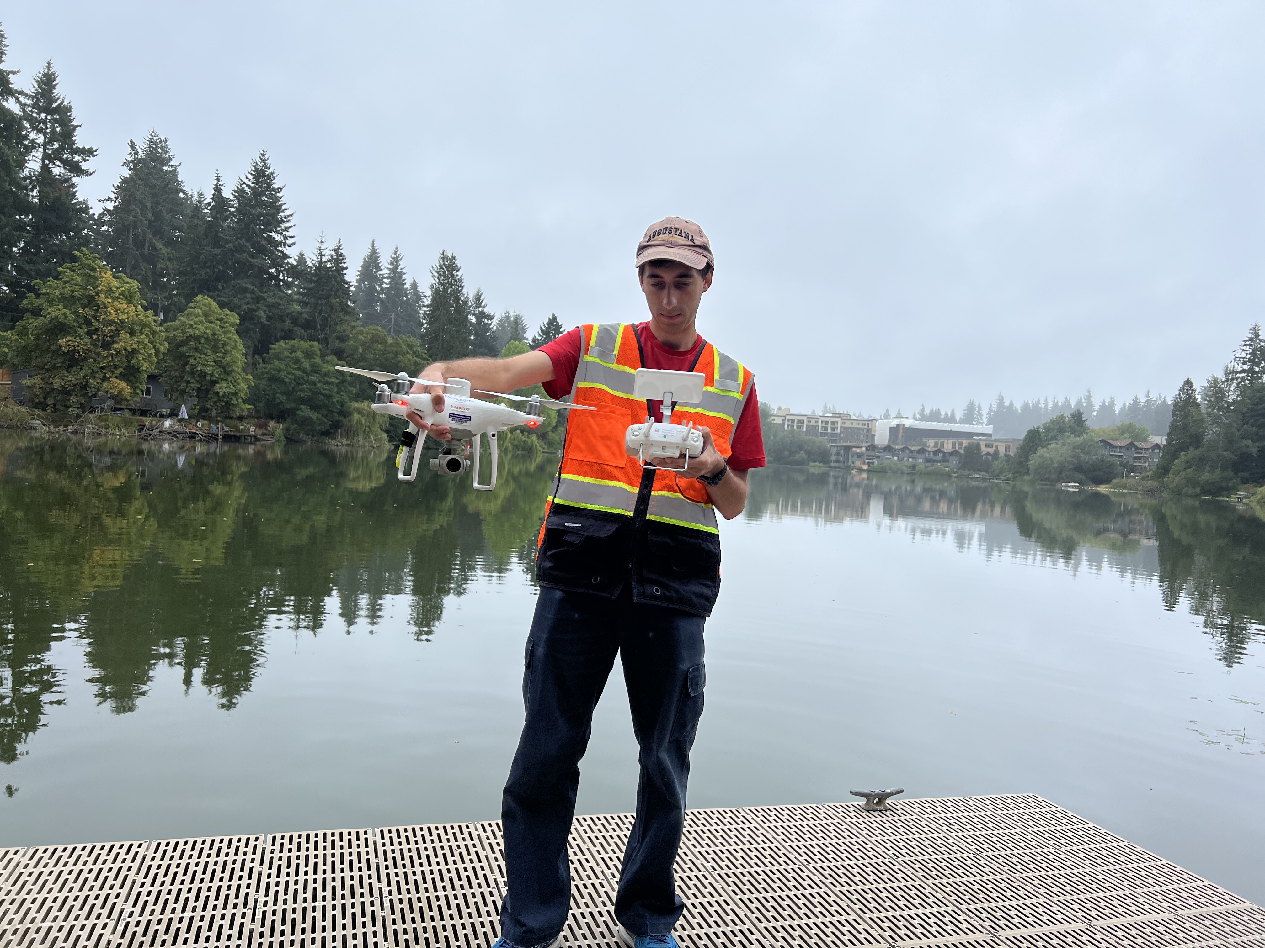 Teresi stands on a dock of a lake holding a remote-operated drone and remote control.