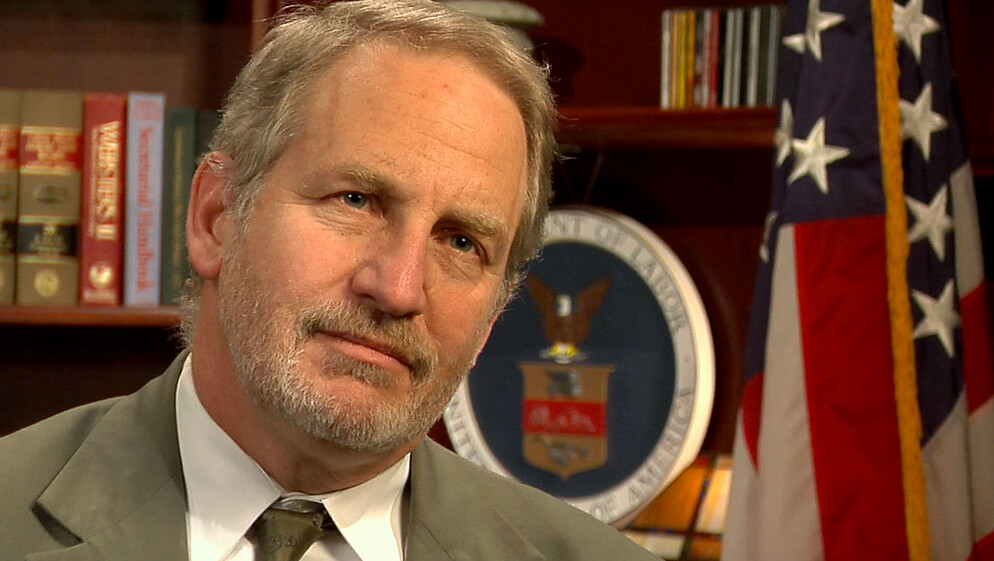 Photo of Jordan Barab in front of the seal of the US Department of Labor and the American flag.