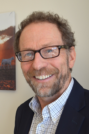 Headshot of Peter Rabinowitz smiling in glasses, a shirt and blazer indoors.
