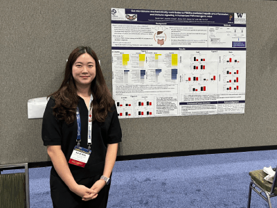 Sarah Kim stands smiling in front of a poster at a conference.