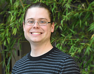 Headshot of Graeme Carvlin standing in front of a green, leafy bush. Photo by Sarah Fish.