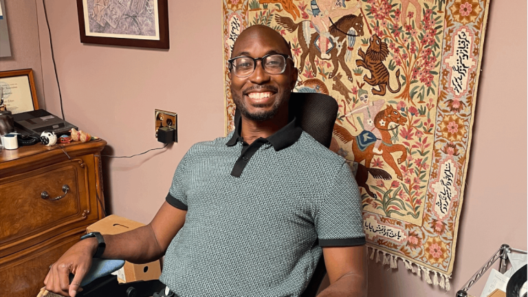 Alawode sits in an office in a clinic with a tapestry behind him.